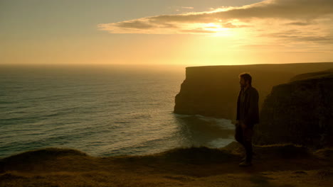 man walking on a cliff at sunset