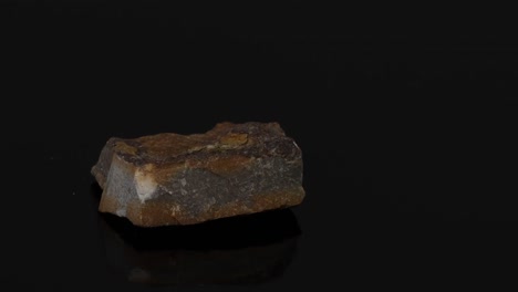 Close-up rotation of a brown rock fragment on a black background, showcasing its texture and shape.