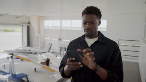 african american avionics technician using mobile phone in hangar