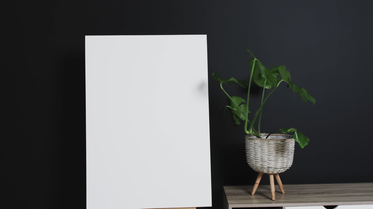 video de un letrero de lienzo blanco en un caballete de madera con espacio de copia y planta en el escritorio sobre un fondo negro