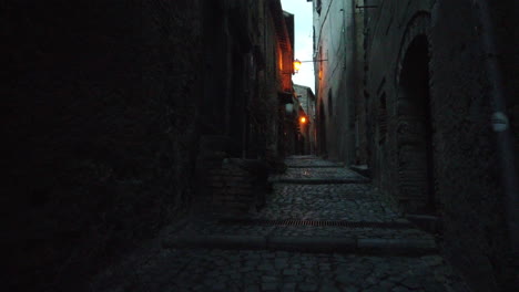 there is a little alley between houses, the road is a stone road by night. we are in a little old town near rome. the place is called bracciano.