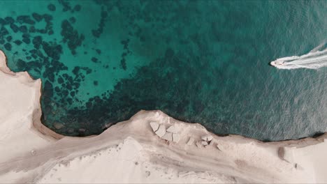 Top-shot-of-patagonian-sea-close-to-the-shore-with-cliffs-and-boat-crossing-from-right-to-left