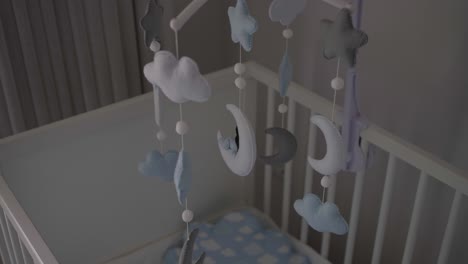 móvil pastel suave con nubes, estrellas y lunas colgando sobre una cuna, creando una atmósfera calmante y soñadora en una guardería