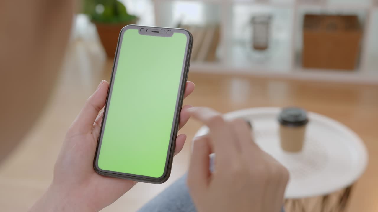 mujer sosteniendo una maqueta de pantalla verde de teléfono inteligente con un mensaje de tipo en el sofá en casa.