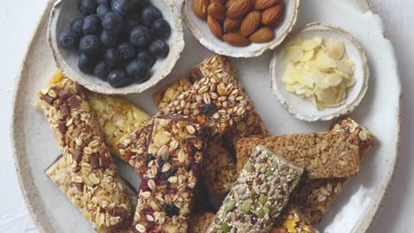 Mixed-composition-of-energy-nutrition-bar--granola-on-ceramic-plate-over-white-background