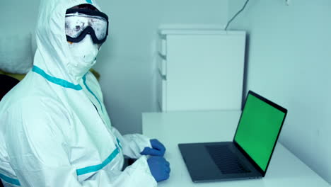 doctor healthcare worker looking from computer green screen to camera in protective mask gear