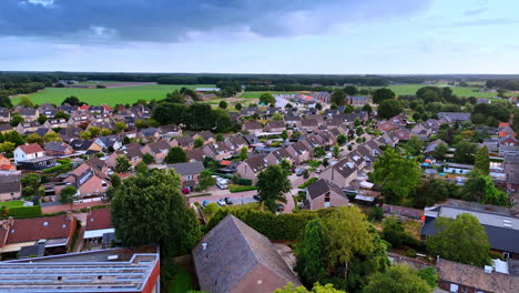 flight over green trees approaching the similar residential houses. lovely town of vierlingsbeek, netherlands on cloudy day