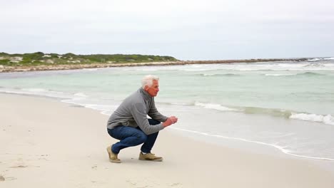 Retired-man-kneeling-on-the-beach-looking-out-to-sea