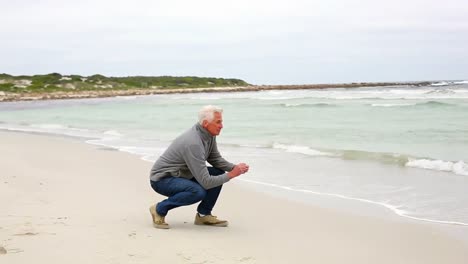 retired man kneeling on the beach looking out to sea