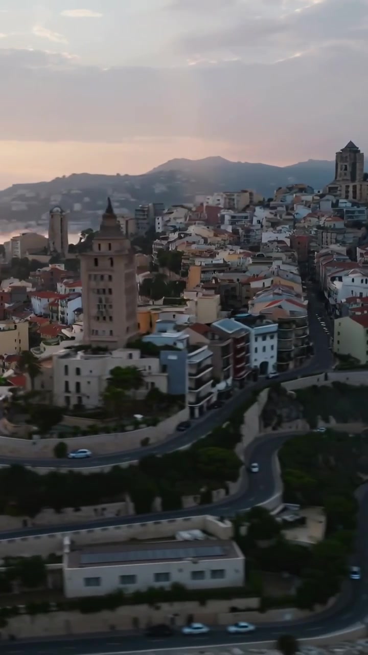 Video verticale: Panoramica ascendente della telecamera che rivela una città costiera, un porto turistico e una chiesa al tramonto.
