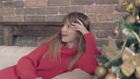 beautiful-young-woman-smiles-on-couch-near-christmas-tree