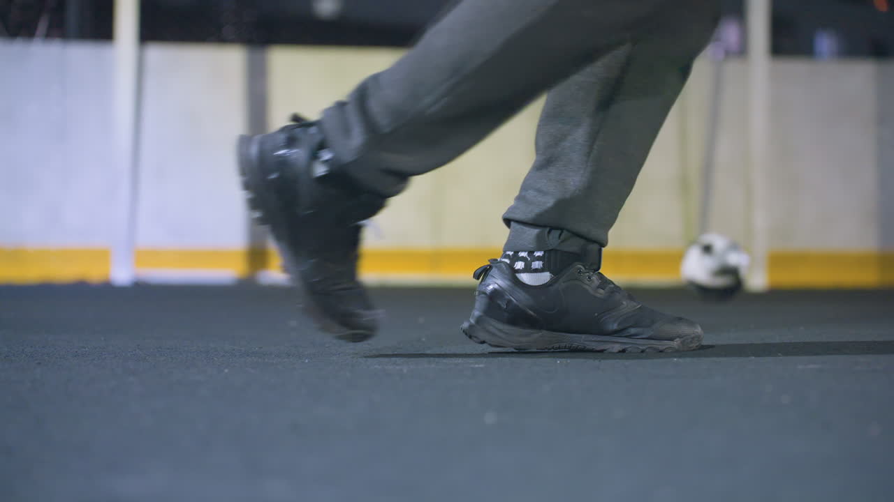 vista trasera de un jugador de fútbol pateando una pelota de fútbol hacia el poste de la portería mientras la pelota rueda, iluminada por la iluminación nocturna brillante en el campo al aire libre, con zapatos atléticos