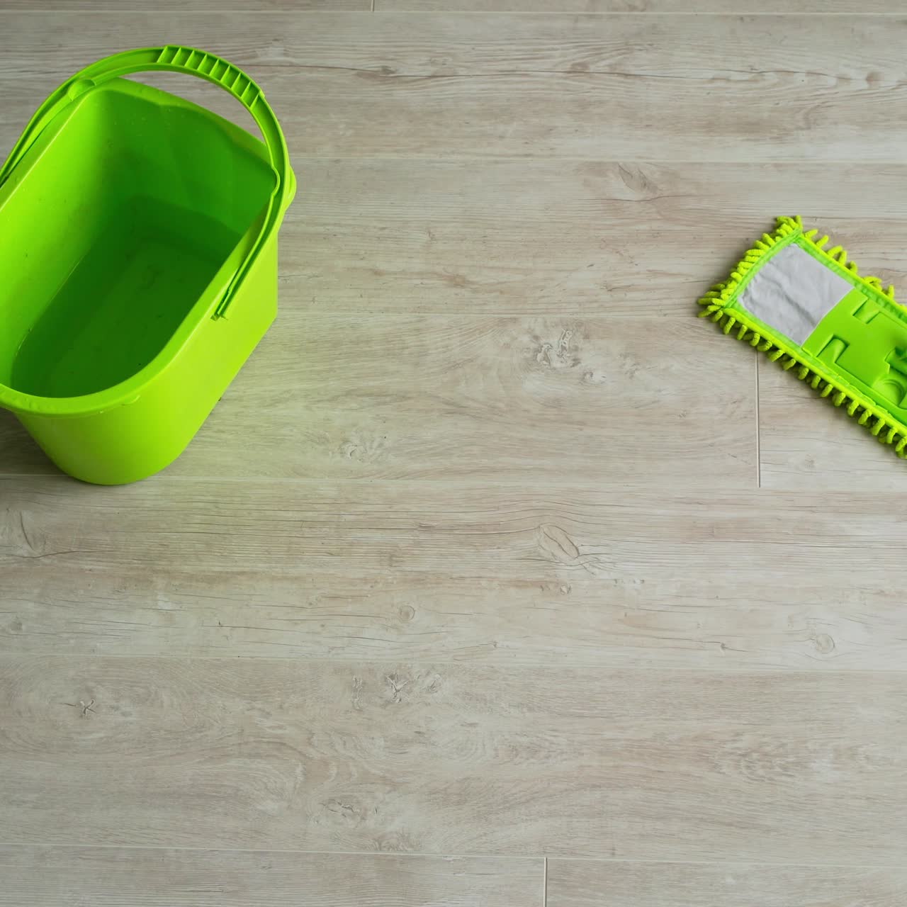 Cleaning the parquet floor with a wet mop. Green brush and a bucket on wooden floor. Housekeeper cleans the floor with a mop. Daily chores in apartment. Top view.