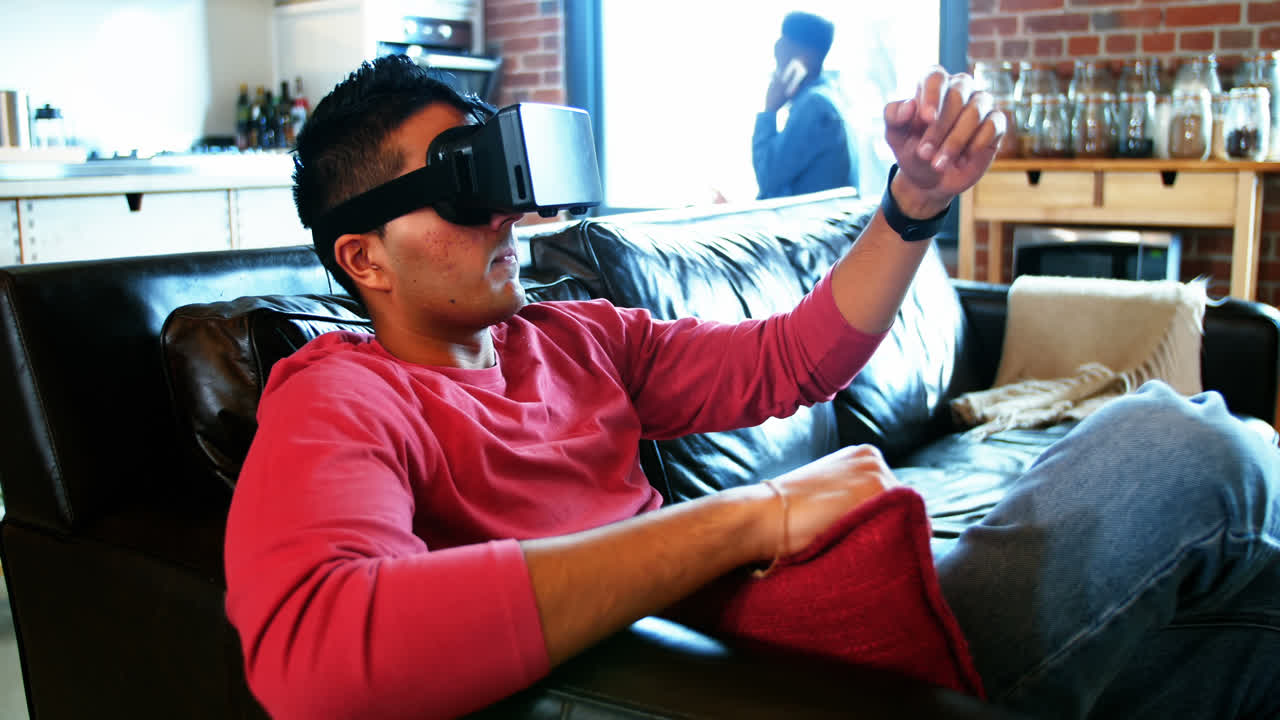 Man using virtual reality headset while friend talking on mobile phone