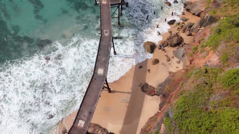 overhead aerial of waves crashing on catherine hill bay shoreline in new south wales below metal structure