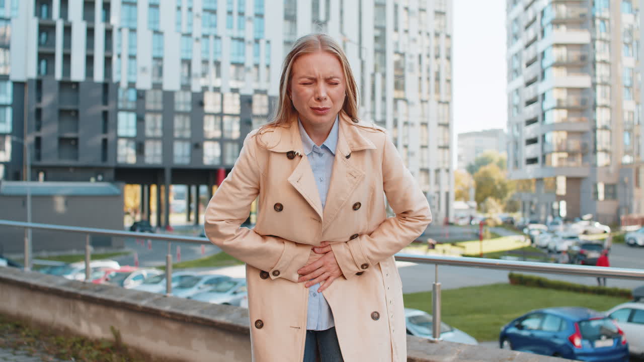 Caucasian mature businesswoman feeling sudden strong abdominal stomach pain problem on city street