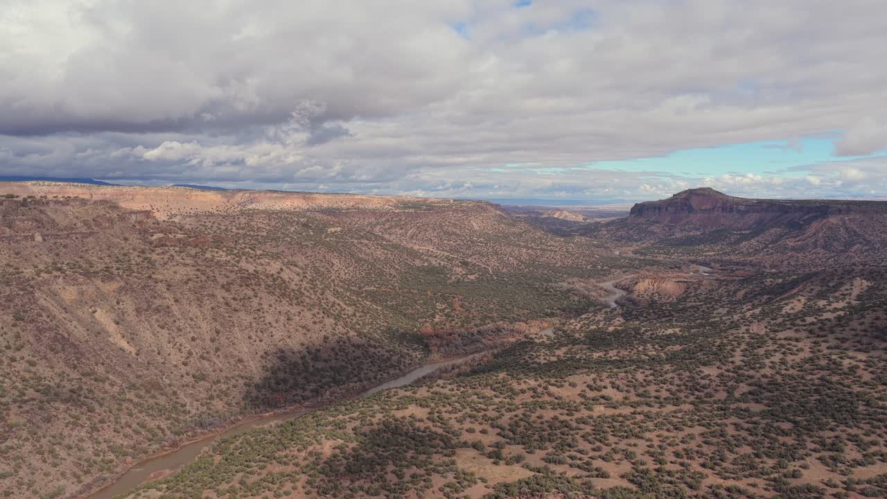 A broad aerial view of the Rio Grande flowing through wide canyon slopes framed by distant mesas and layered desert hills