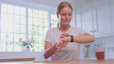 mujer madura usando ropa de fitness en casa en la cocina registrando actividad en una tableta digital