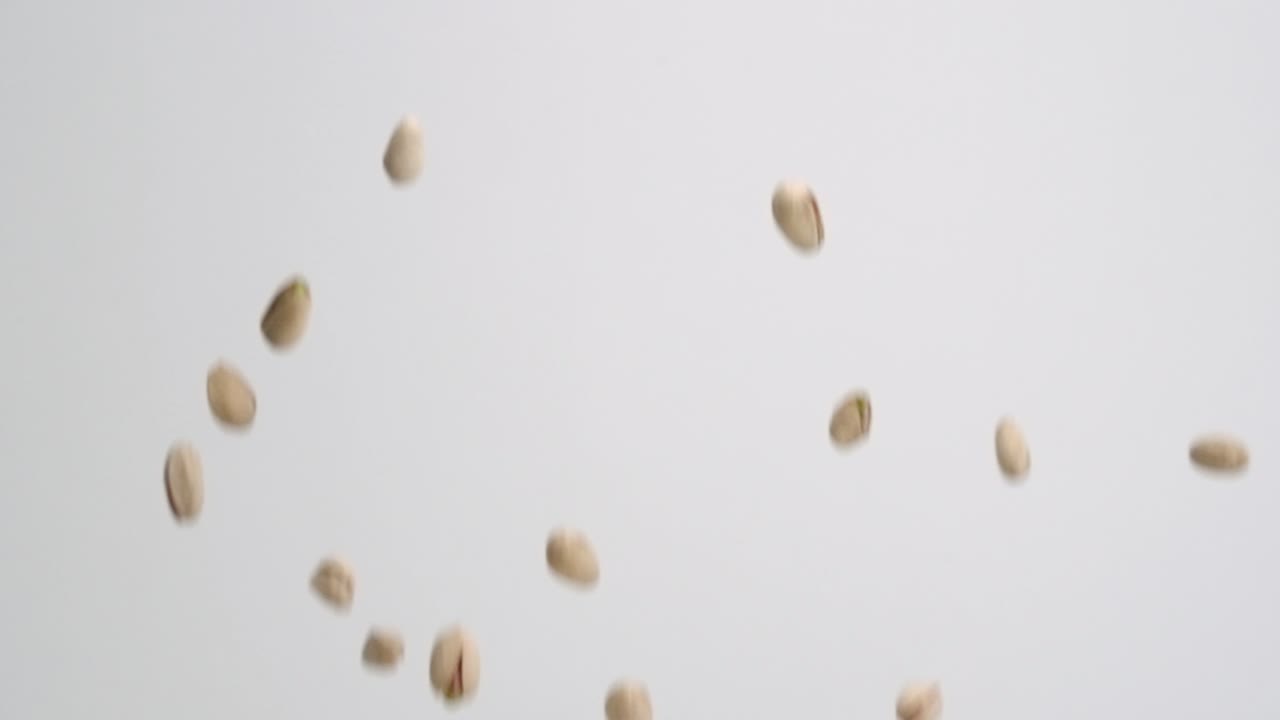 nueces de pistacho enteras en conchas que se elevan sobre fondo blanco en cámara lenta