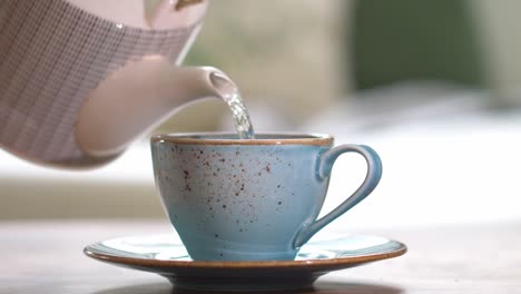 pouring fresh herbal tea out of beautiful tea pot into blue tea cup