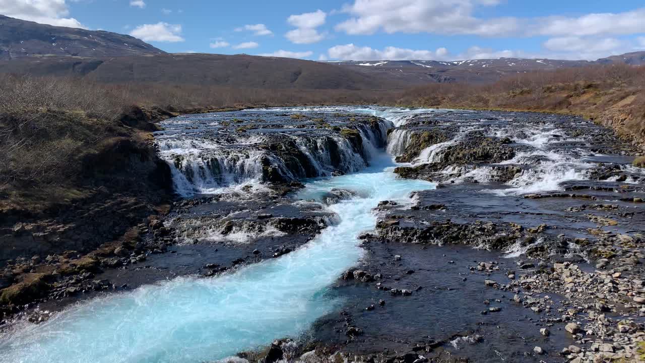 View over the beautiful waterfall Bruarfoss with Icelands most turquoise water, watching the water pouring from the rocks with the majestic Icelandic landscape surrounding the water