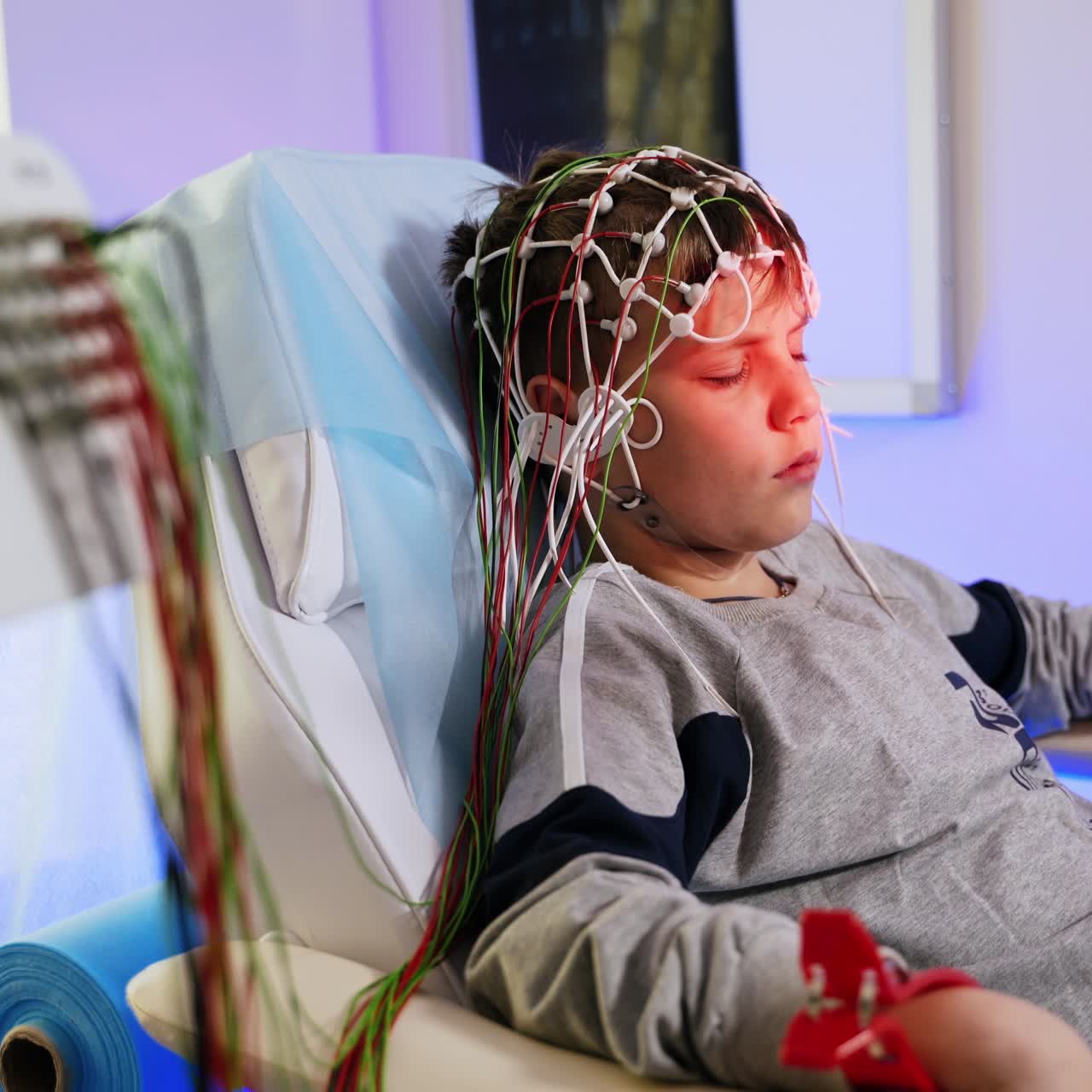 Boy sits leaned back in the chair. Teenage patient having sensors on his head undergoing EEG check up
