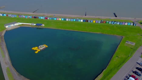 Aerial-Orbit-of-Dovercourt-Boating-Lake-with-Colorful-Beach-Huts-in-the-Background