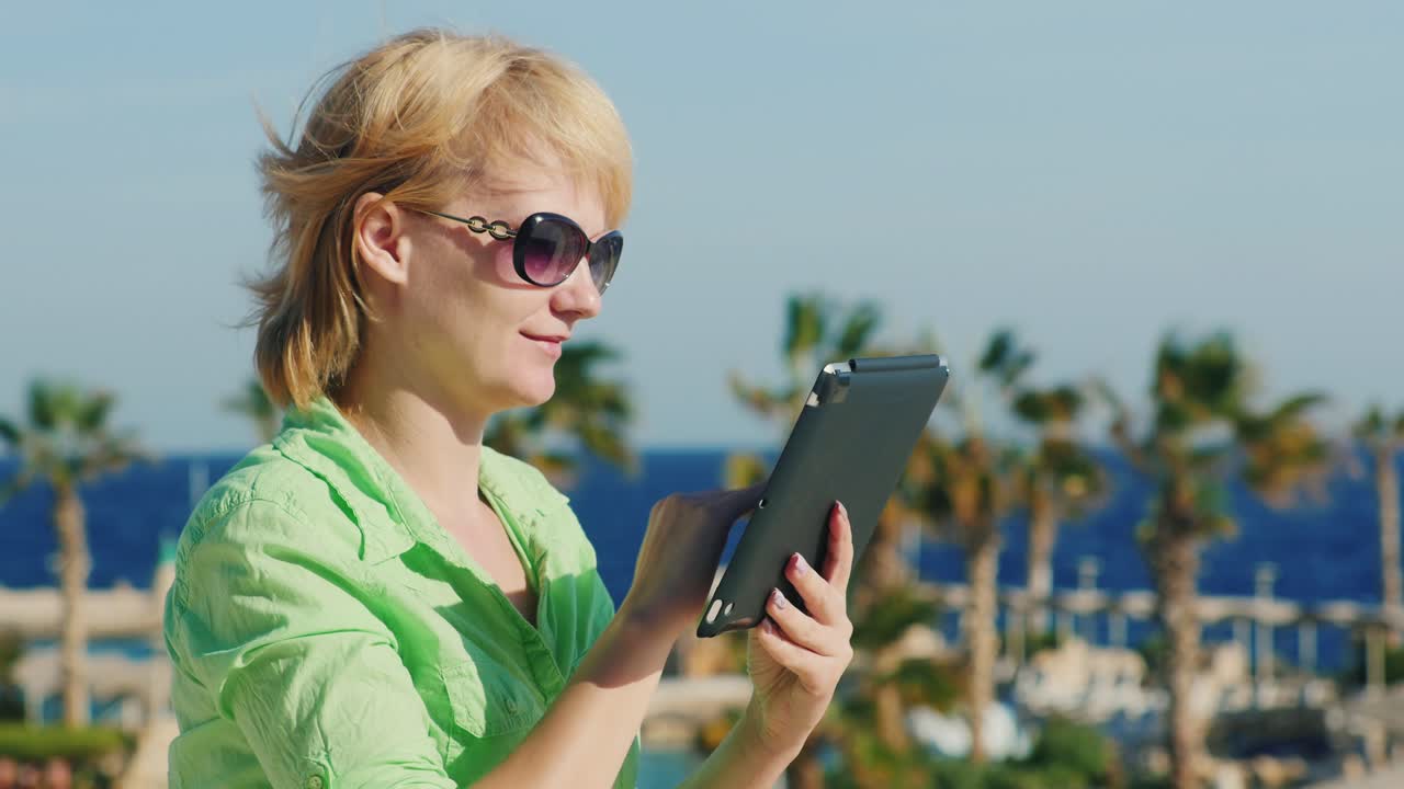 A Tourist In Sunglasses Enjoys The Tablet On A Background Of A Tropical Landscape