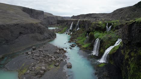 an aerial view of a canyon in the icelandic highlands, showcasing a blue river flowing through its depths with waterfalls cascading down the rugged canyon walls into the river below.