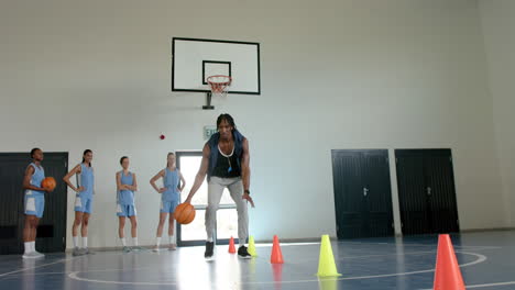 dribbling basketball around cones, coach training female basketball team in gym