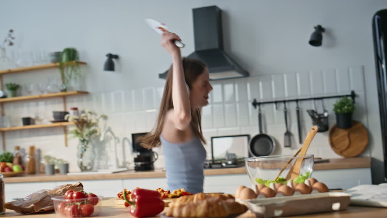 Ragazza con cuffie che cucina e balla allegramente in una cucina moderna. Donna che ascolta
