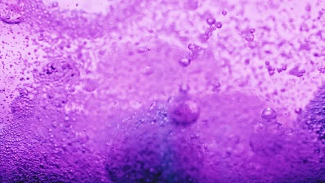 macro shot of violet bubbles dripping and moving around in bright violet water