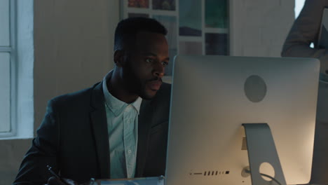 african american businessman working late using computer writing notes brainstorming ideas planning project deadline in office workspace