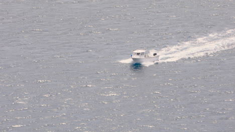 small white fishing boat crosses calm water on bright summer day