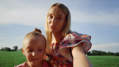 Smiling-mother-and-daughter-posing-for-mobile-phone-camera-in-city-park.