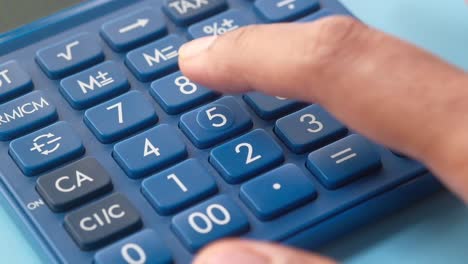 close-up of a hand pressing a button on a blue calculator