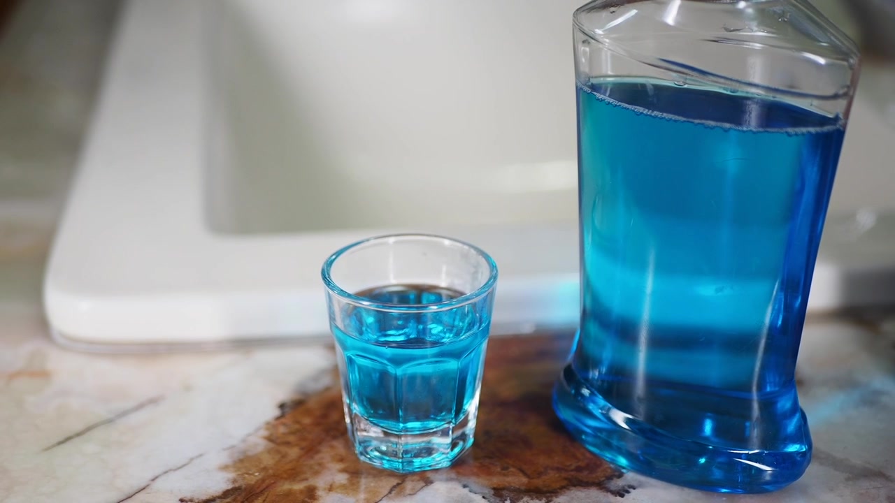 Nước súc miệng màu xanh trong chai và ly nhỏ trên kệ phòng tắm
