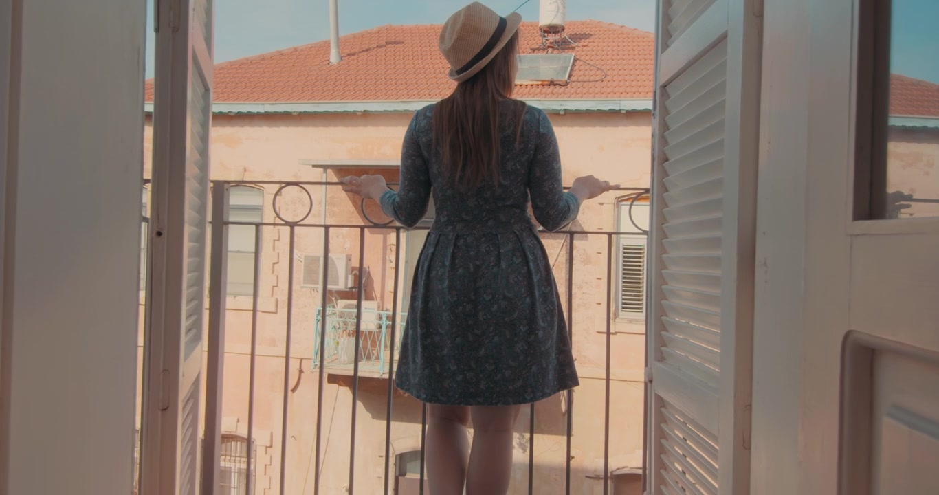 Frau mit Hut blickt vom Balkon