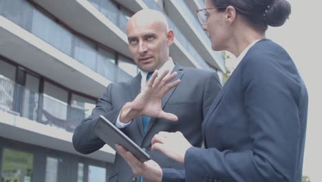 two business partners discussing project using tablet while standing near office building outside