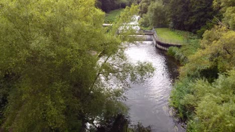 Aerial-revealing-shot-of-the-small-water-dam-hidden-in-the-woods-on-the-Little-Ouse-river-near-Thetford-in-the-UK