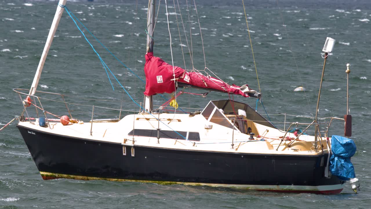 Moored sailboat sways in windy conditions, midday sunlight, medium telephoto shot, stable camera