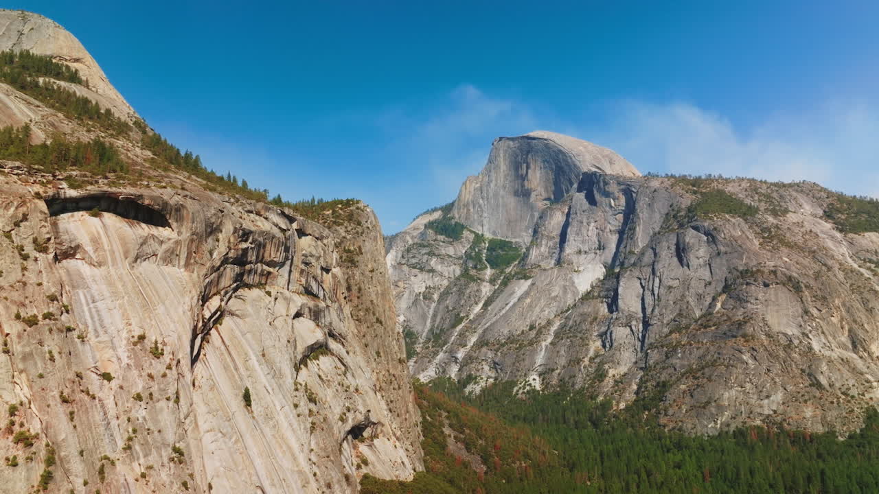 Slow motion approach to the cliffs in Yosemite National Park, California, USA. Pine tree wood growing at the foot of mountain.