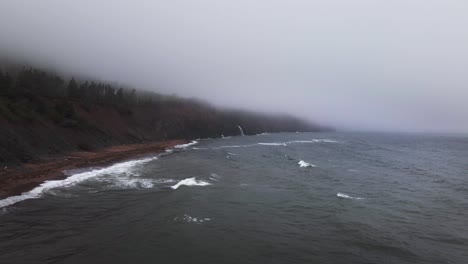 drone shot approaching a massive coastal waterfall located in the deep wilderness of cape breton highlands in nova scotia, canada shot during a cold and rainy summer day