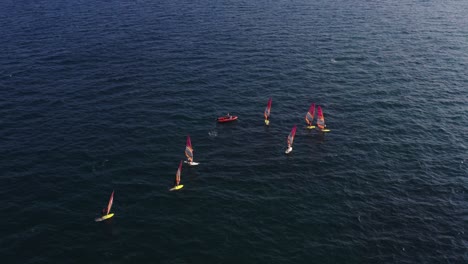 Grupo-De-Windsurfistas-Con-Tablas-De-Surf-Amarillas-Y-Blancas-Reunidas-Alrededor-De-Una-Lancha-Naranja-En-El-Mar-Mediterráneo-Cerca-De-Herzeliya