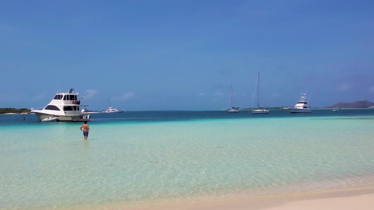 Man walking man on shallow caribbean sea water to yacths, luxury vacation lonely beach
