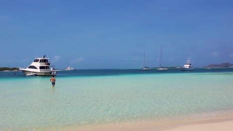 Man-walking-man-on-shallow-caribbean-sea-water-to-yacths,-luxury-vacation-lonely-beach