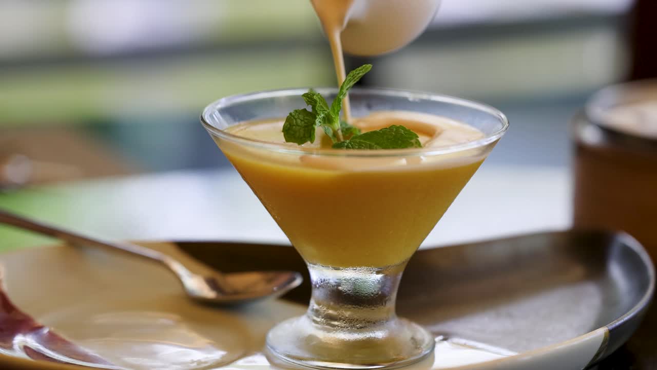 un primer plano de la crema que se vierte sobre un postre tailandés, destacando la rica textura y la presentación vibrante