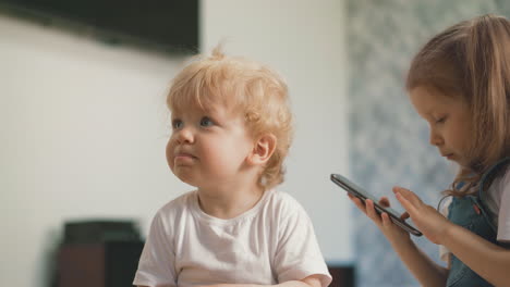 little boy in white t-shirt sits near sister with cellphone