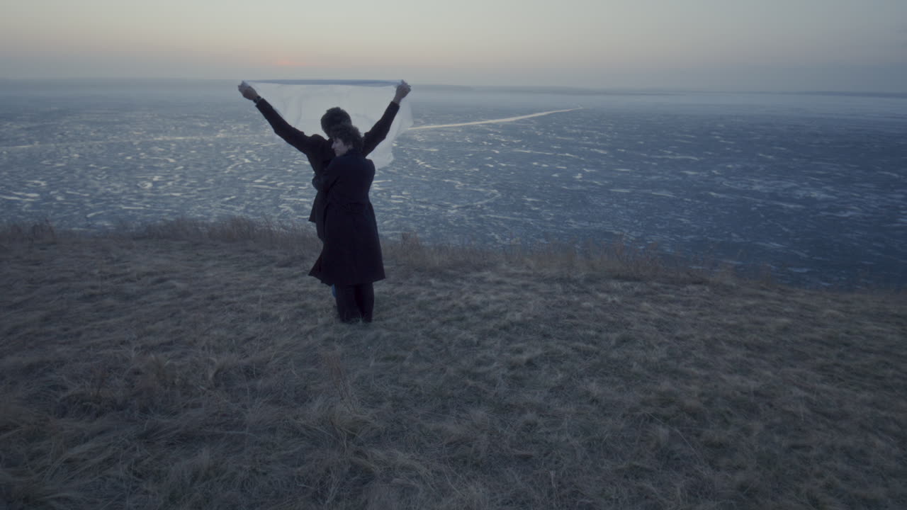 Woman Hugging Boyfriend as He Holding Flowing Fabric above Frozen Lake