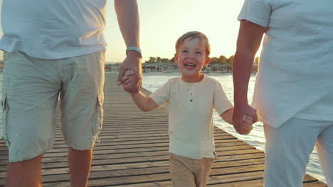 happy boy walking with grandparents along the pier at sunset